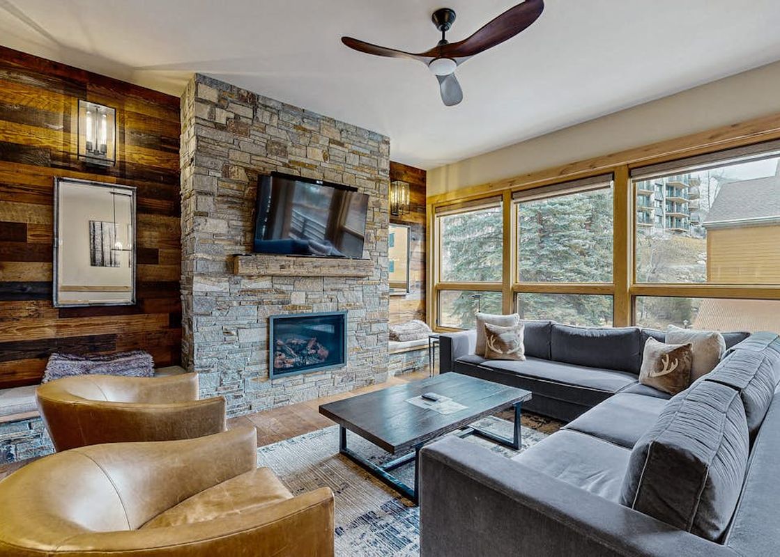 Cozy living room in Kutuk 211 featuring a stone fireplace, gray sectional sofa, and scenic mountain views.