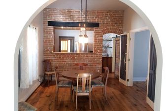 The dining room of Turn of the Century Gem on the Park features an exposed brick wall, a wooden table, four chairs, and a wood floor.