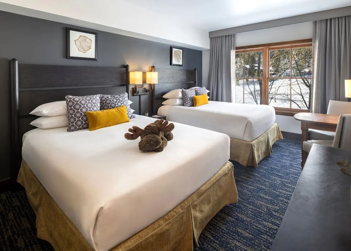 Cozy hotel room at Teton Mountain Lodge and Spa featuring two queen beds, alpine-inspired decor, and a window viewing snowy trees.