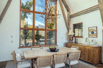 A dining room with a large window overlooking a forest and mountains