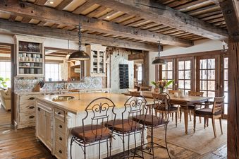 A rustic-style kitchen with a large wooden beam ceiling, a spacious island with bar stools, and an adjacent dining area.