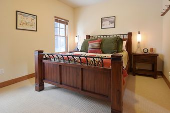 A cozy bedroom at Rendezvous 25 Discovery Lane with a large wooden bed, nightstand, and window.