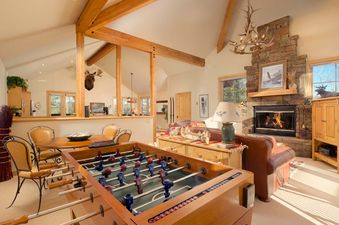 Cozy rustic living room in Moose Creek 31 with a stone fireplace, foosball table, and comfortable leather seating.