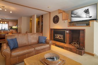 The living area at Iron Horse J1309 features a comfortable leather sofa, a brick fireplace, and a large wall-mounted television.
