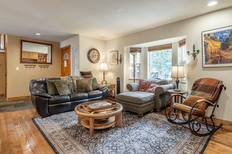 A cozy and inviting living room at the North Shore Forest Haven, featuring a leather sofa, armchair with ottoman, wooden coffee table, and a unique rocking chair, all set on a patterned area rug.