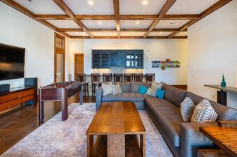 A spacious entertainment lounge at Ridgepoint Retreat features a large sectional sofa, a foosball table, a television, and a wet bar.