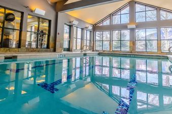An expansive indoor swimming pool at Teton Mountain Lodge and Spa with vaulted ceilings, large windows showcasing mountain views, and an adjacent fitness center.