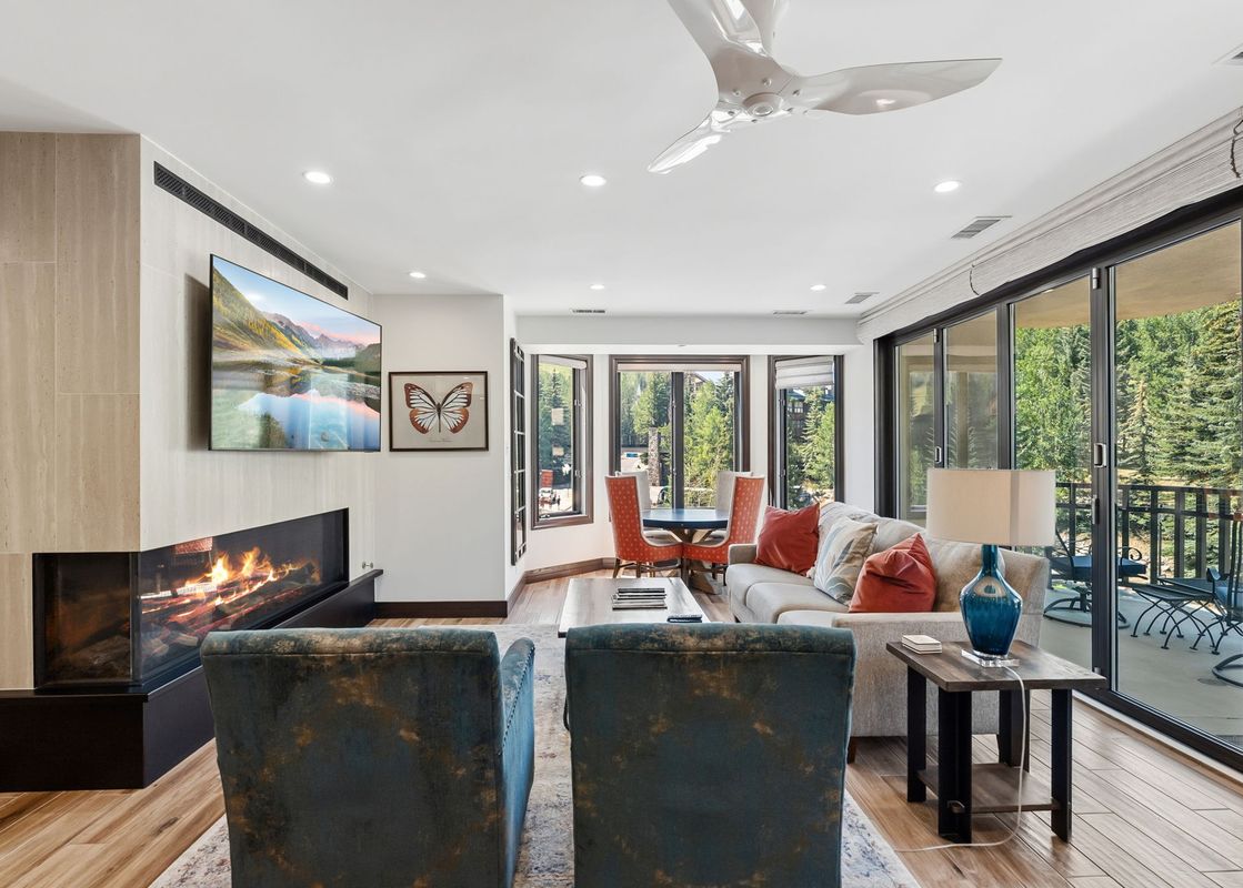 Living area in 421 Beaver Creek Lodge featuring a modern fireplace, stylish armchairs, a sofa, and sliding doors to a balcony with forest views.