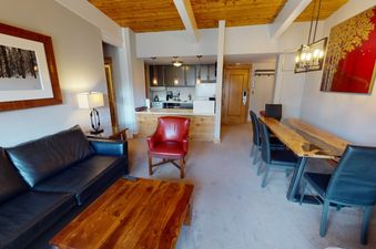 The living room at Manor Vail 382 features a leather sofa, coffee table, red armchair, and a large dining table.