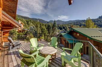 The deck of Snowridge Chalet 7 offers stunning mountain views from a spacious outdoor area furnished with green Adirondack chairs and a wooden table.