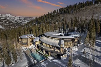 An aerial view captures the stunning Alpine Opus amidst a snow-covered mountain landscape, with a vibrant sunset illuminating the sky.