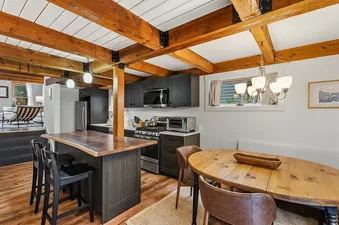 Rustic and modern kitchen and dining area at Town Charm featuring exposed wood beams, a central island, and a wooden dining table.
