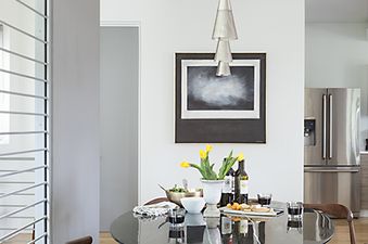 A modern dining area in The Jackson View with a dark round table, wooden chairs, a multi-tiered pendant light, and abstract art on the wall.