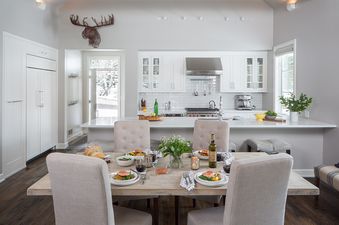 The open-concept kitchen and dining area features white cabinetry, stainless steel appliances, a subway tile backsplash, a large kitchen island, and a dining table set for a meal.