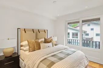 The primary bedroom at Mears Station B showcases a king-sized bed with an upholstered headboard, elegant bedding, and a sliding glass door leading to a balcony.