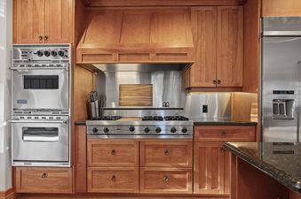 The kitchen in 7780 Sterling Drive features wooden cabinetry, stainless steel appliances, a gas range with a custom hood, and dark granite countertops.