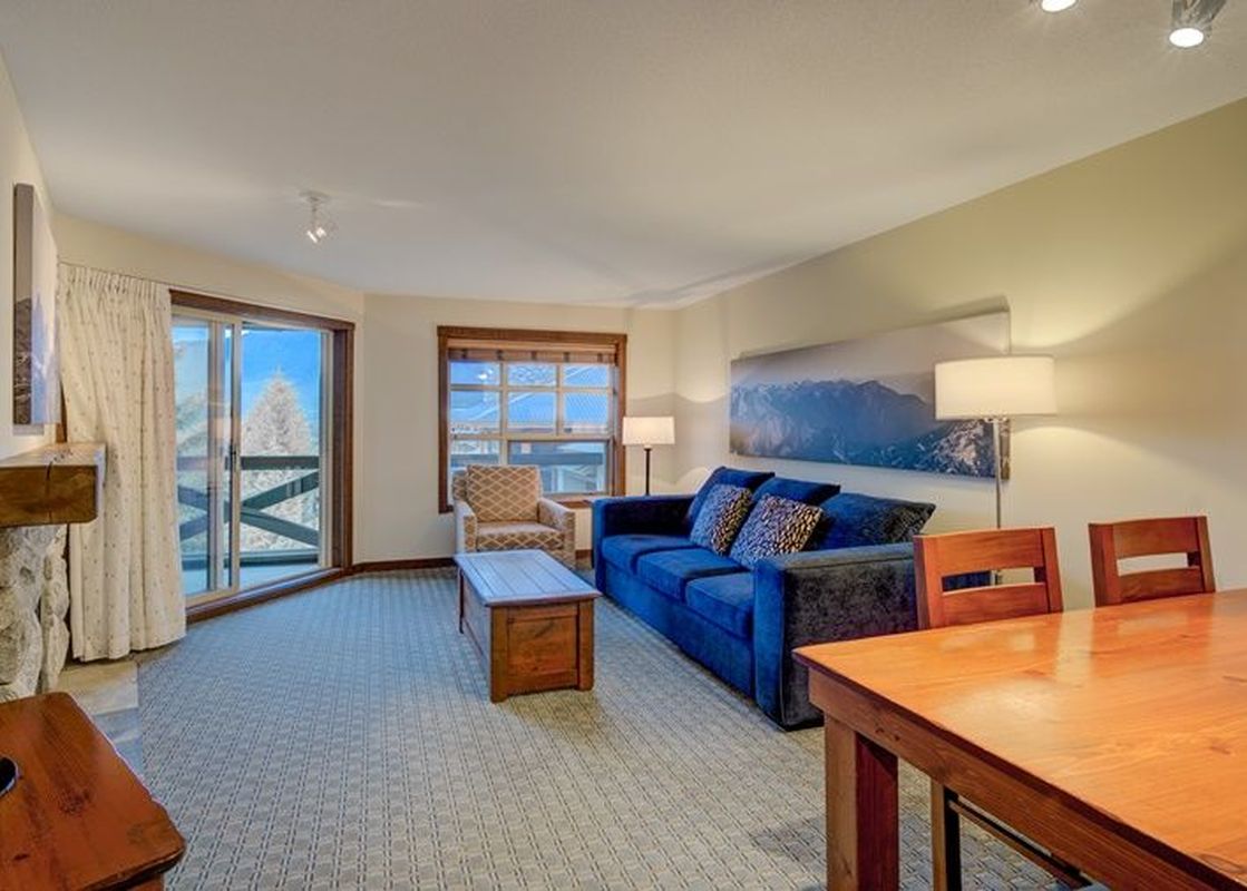 A living area in Blackcomb Springs One Bedroom Slopeside with a stone fireplace, blue sofa, and dining area.