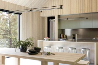 A modern open-concept kitchen and dining area with light wood paneling, a large wooden table with benches, and a kitchen island with bar stools.
