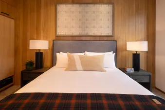A comfortable bedroom with a queen-sized bed, wood-paneled walls, and two bedside tables with lamps, inviting a restful stay in The Sylvan Lodge Four Bedroom Penthouse.