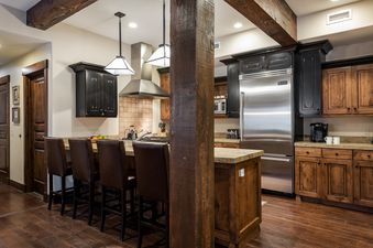 A gourmet kitchen with dark wood cabinetry, stainless steel appliances, a kitchen island with bar seating for four, and exposed wooden beams overhead.