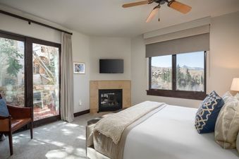 The Lumiere Four Bedroom Residence features a spacious master bedroom with a fireplace, large windows with mountain views, and a cozy sitting area.