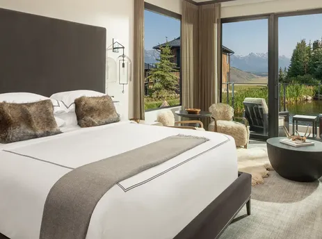 A luxurious bedroom and lounge area in the Grand Reflection Suite with floor-to-ceiling windows offering scenic mountain and pond views.