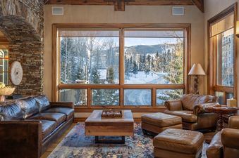 A cozy living room with leather furniture and large windows looking out onto a snow-covered mountain landscape.