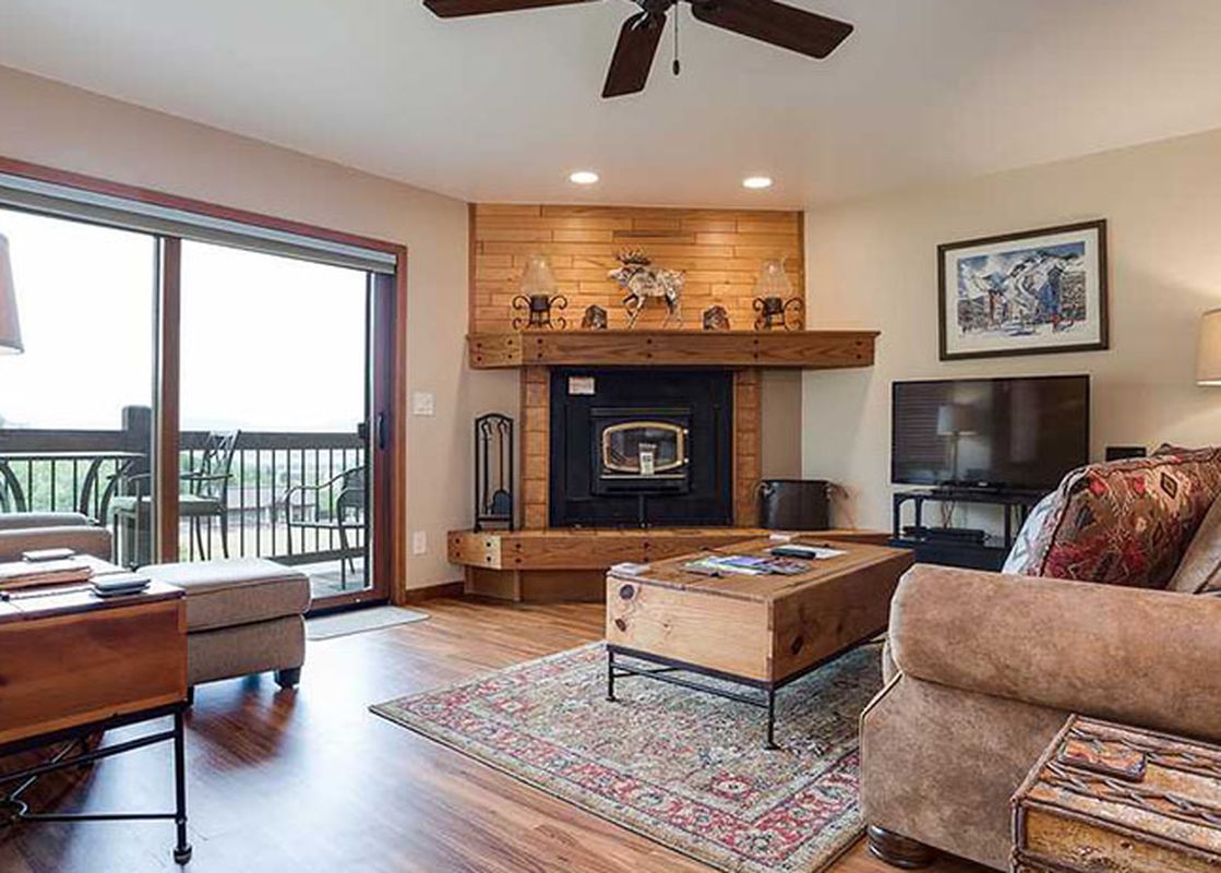 A cozy living room with a fireplace, a brown sofa, a rustic coffee table, and a balcony with an exterior view at Ranch at Steamboat RA307.