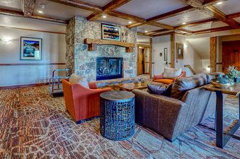 The living room of EagleRidge Lodge 211 features a large stone fireplace with a flatscreen TV, wood beam ceilings, and unique upside-down furniture. The room has a spacious and open layout.