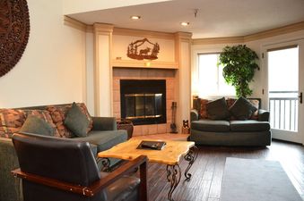 A living room with a fireplace, couch, and a large window with a view of the mountains.