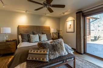 A master bedroom at the Abode at Sage Springs showcases a cozy ambiance with a large bed, decorative pillows, and a private patio.