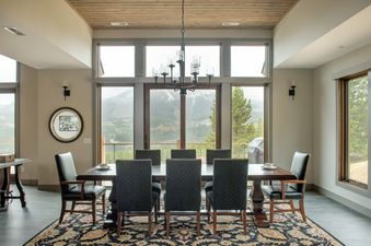 A spacious dining room with a large wooden table, multiple chairs, and expansive windows offering a scenic mountain view.