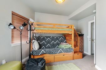 A cozy children's bunk room at Alpine Village 3 features a wooden bunk bed with a futon below, a multi-headed floor lamp, and a window with blinds, creating a comfortable and functional space.