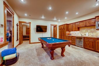 A spacious recreation room with a billiards table, wet bar, and multiple doorways leading to other areas of the lodge.