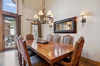 A large wooden dining table with eight chairs, a chandelier, and a mirror in Villa Montane 226's dining room.
