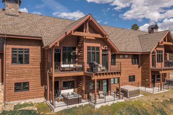 A multi-story condo building with a warm wood exterior, multiple balconies with outdoor seating and grills, and two ground-level hot tubs under a blue sky.