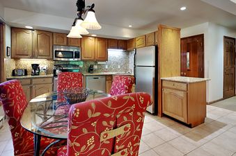 Kitchen and dining area in the Timberline Two Bedroom B2E with glass dining table, red patterned chairs, and wood cabinetry.