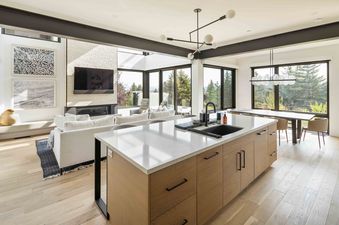 The kitchen in Canyons Edge features modern cabinetry with sleek black hardware, a large island with a white countertop and a stainless steel sink, and a large window with views of the trees outside.