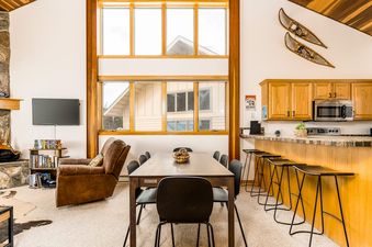 A spacious great room in Big Horn 65 with a dining table, a living area with a TV and a brown recliner, and a kitchen bar with stools.