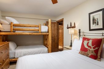 A cozy bedroom at Montaneros 308 features rustic wooden bunk beds, a queen-sized bed with a deer-themed accent pillow, and warm lighting.