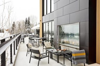 Outdoor patio at Gravity Haus JH Deluxe Loft featuring a modern glass fireplace and dining tables against a winter mountain backdrop.