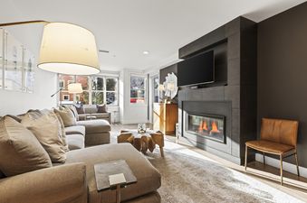 A modern living room features a large sectional sofa, a unique wooden coffee table, and a dark fireplace with a mounted television.