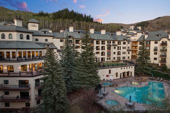 An elevated, wide-angle view of the Charter resort at dusk, featuring the buildings, swimming pool area with several hot tubs, and surrounding pine trees and mountains.