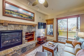 Living area in EagleRidge Lodge 311 with a stone fireplace, leather sofa, and sliding glass door leading to a balcony.