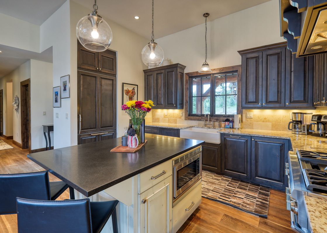 A modern kitchen with dark wood cabinets, granite countertops, and a central island with bar stools and a built-in microwave.