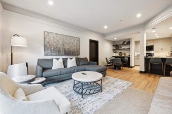 An expansive open-concept living area at The Charter D3105, featuring a gray sectional, cream armchair, dining nook, and a modern kitchen with light cabinetry.