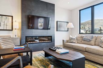 One Riverfront Condo 203 living room features a fireplace, a large flat screen TV, a sofa, two chairs, and a coffee table.
