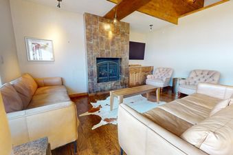 A living room with a fireplace, couches, and coffee tables, a brown leather couch is seen in the foreground.