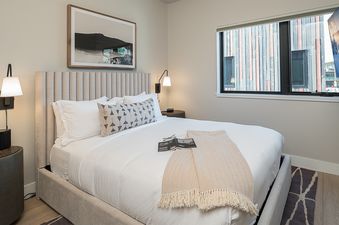 A cozy bedroom with a large bed, wall sconces, a window, and a wall-mounted TV.