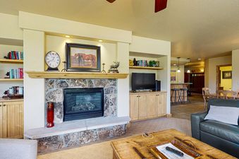 A cozy living room at Torian Plum Creekside 519, featuring a warm stone fireplace, a large flat-screen TV, and comfortable seating, all bathed in natural light.